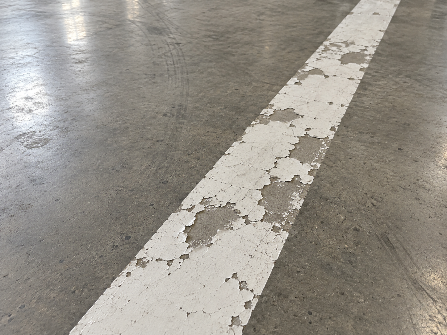 Sert beton zeminde tutunmasını kaybederek tabaka hâlinde soyulan beyaz yol çizgisi