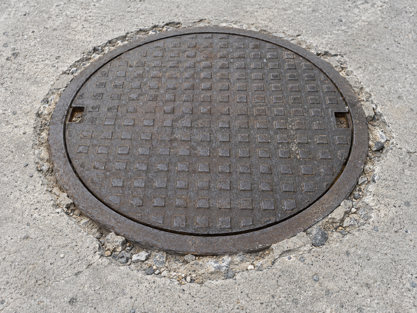 Kapalı rögar kapağının sağlam metal çerçevesi çevresinde kırılmış beton kenarlar